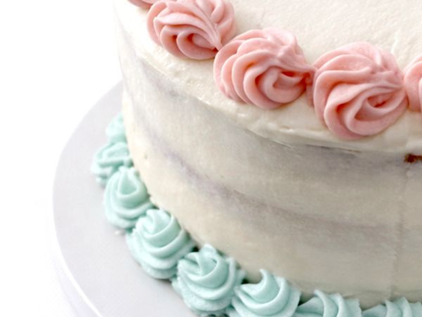 A layered cake with blue shells bordering the bottom layer, pink rosettes bordering the top layer.