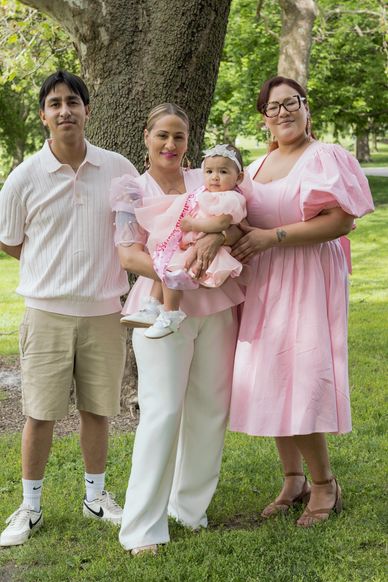Family posing outdoors with baby in pink dress.