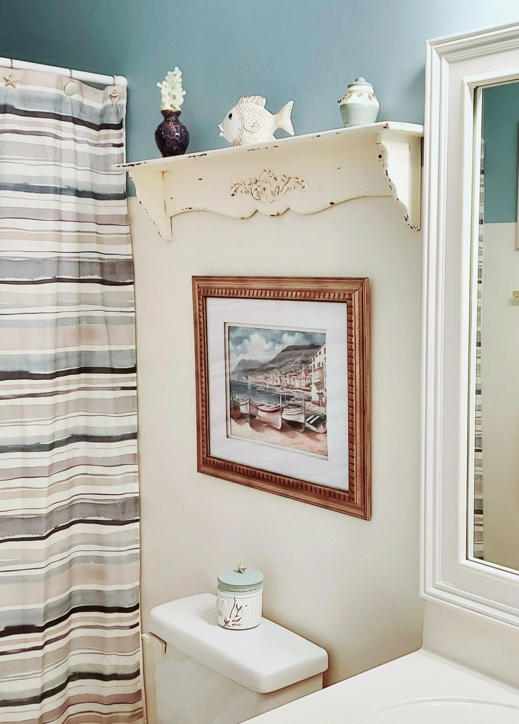 Coastal-themed bathroom with framed boat artwork and decorative shelf.