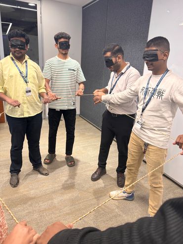 Four blindfolded men holding a rope in an office setting.