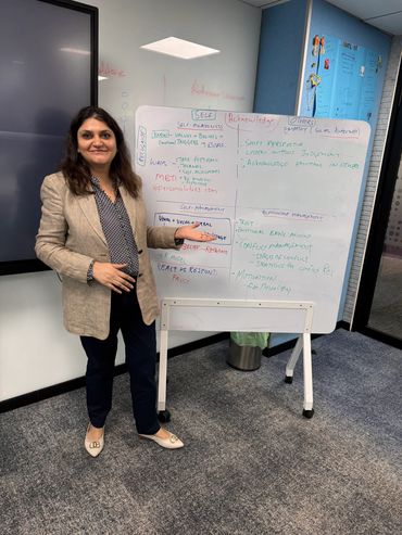 A woman presenting a whiteboard with notes on self-awareness and empathy in an office setting.