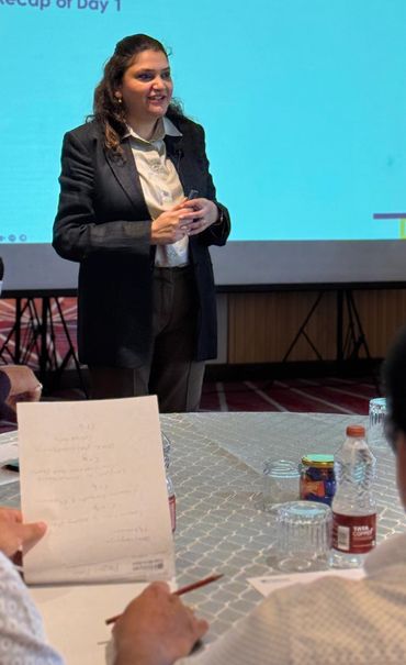 Woman in a black blazer presenting in front of a screen during a meeting.