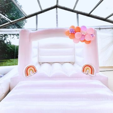 Pastel pink bouncy castle with rainbow decorations and balloons.