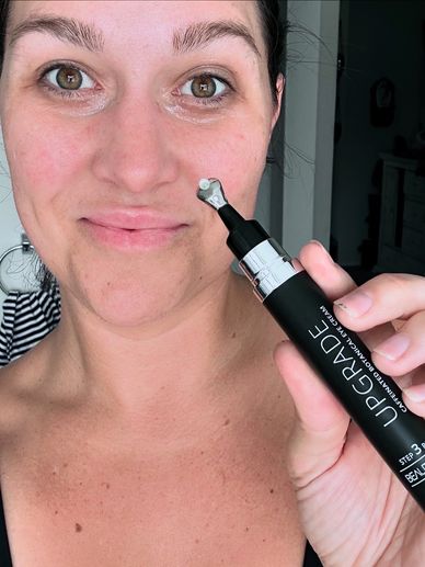 Stephanie holding Beauty Society Upgrade eye cream near her face with no makeup.