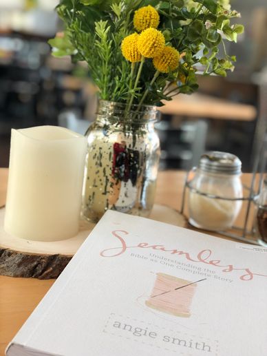 Bible study book "Seamless" by Angie Smith on a table next to a candle and yellow flowers in a jar.
