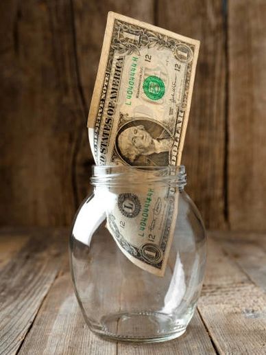 One dollar bill in a small glass jar on a wooden table background.