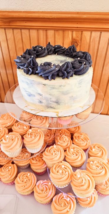 A cake with black frosting and matching peach cupcakes on a tiered stand.