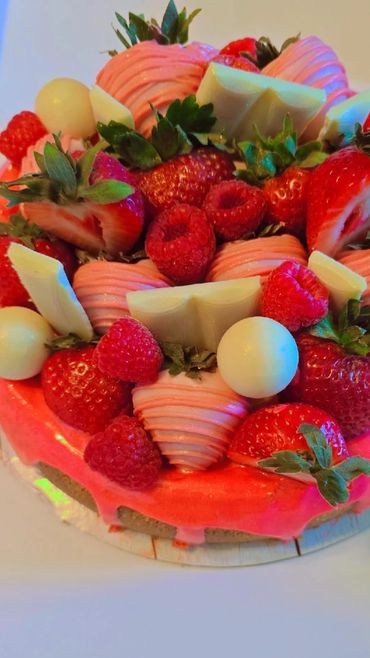 A vibrant cake topped with strawberries, raspberries, white chocolate, and pink frosting.