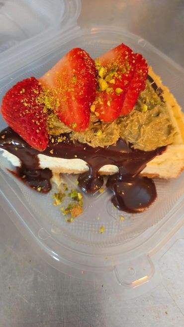 Slice of cheesecake topped with chocolate, strawberries, and crushed pistachios.