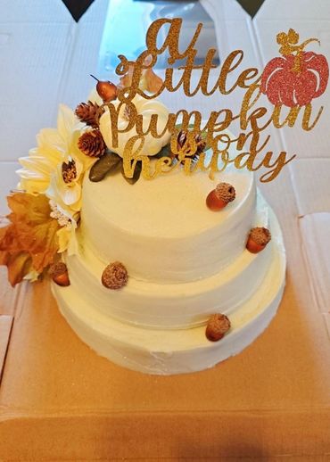 Two-tiered autumn-themed cake with "A Little Pumpkin on Her Way" topper.