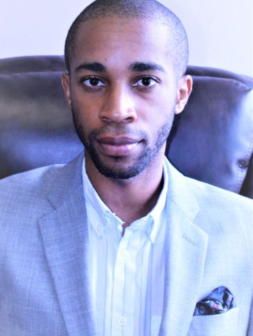 Young man in a light gray blazer sitting on a leather chair.