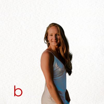Smiling woman in white dress with long hair against textured white background.
