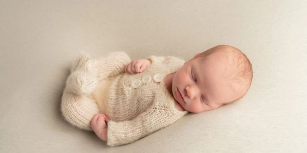 A newborn baby peacefully sleeping in a knitted cream outfit.