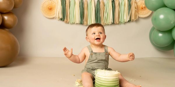 Happy baby sitting with a cake, smiling joyfully.