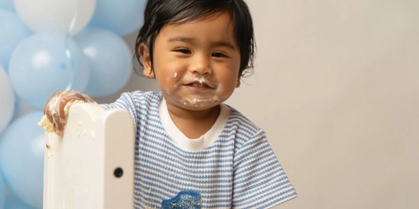 A toddler with a messy face smiling near balloons.