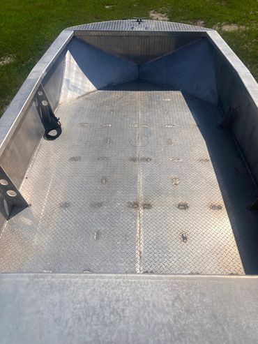 Empty metal boat with diamond plate flooring on grass.