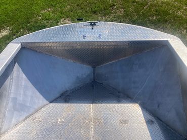 Empty aluminum boat on grass with diamond plate flooring.