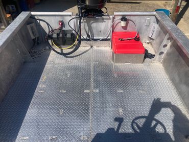 Interior of a metal boat with a red fuel tank and motor.