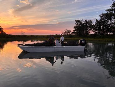 Two men on a boat at sunset surrounded by calm water and trees.
