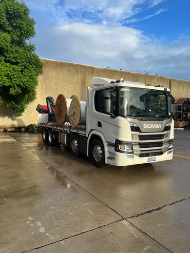 White Scania truck with large reels on flatbed in industrial area.