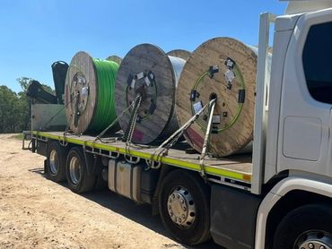 Flatbed truck carrying large industrial cable reels secured with chains.