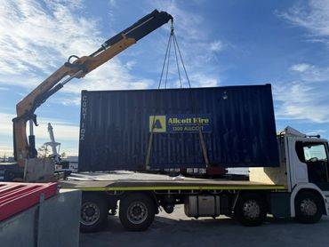 A crane lifting a large blue shipping container onto a truck.