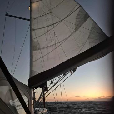 Sailboat at sunset with sails catching the wind over the ocean.