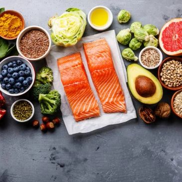 Fresh salmon fillets surrounded by healthy fruits, vegetables, and nuts on a grey background.