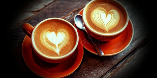 Two cups of coffee with heart-shaped latte art on wooden table.