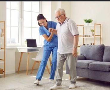 Nurse assists elderly man to walk safely inside a bright living room.