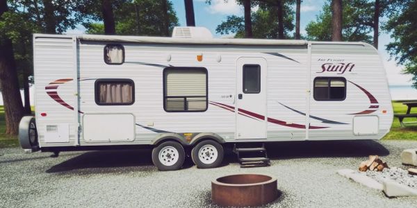 White travel trailer parked near trees and fire pit.
