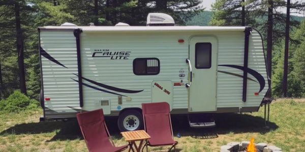 A white travel trailer with two chairs and a fire pit outside.