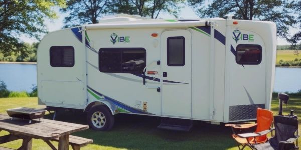 White Vibe RV parked by a lake with camping setup.