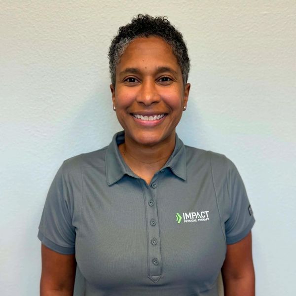 Smiling woman in a gray polo with Impact Physical Therapy logo.