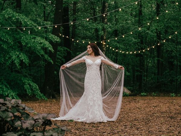 Bride in a lace wedding dress with veil outdoors under string lights.