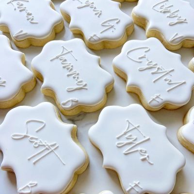 White frosted cookies with names written in cursive icing.