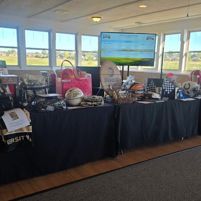 A table displays various sports memorabilia for a charity auction in a bright room.