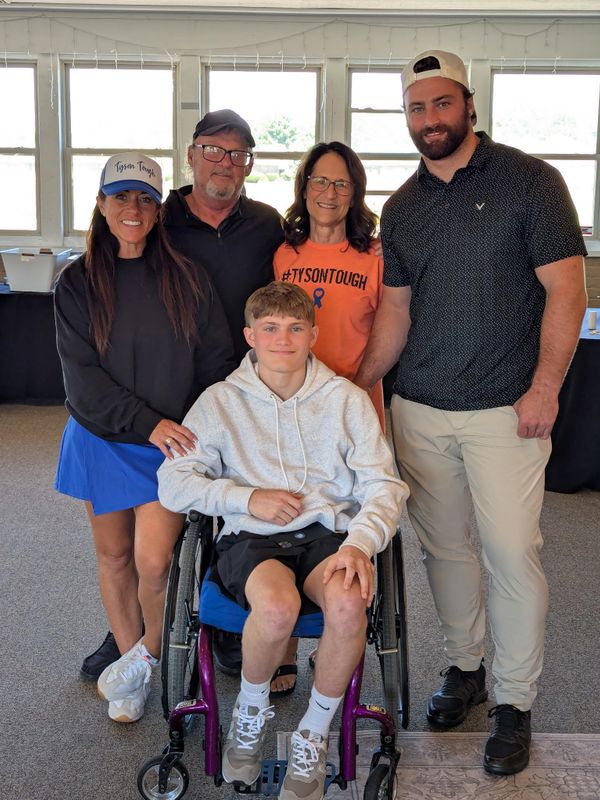 Group photo of five people, including a young man in a wheelchair, smiling indoors.