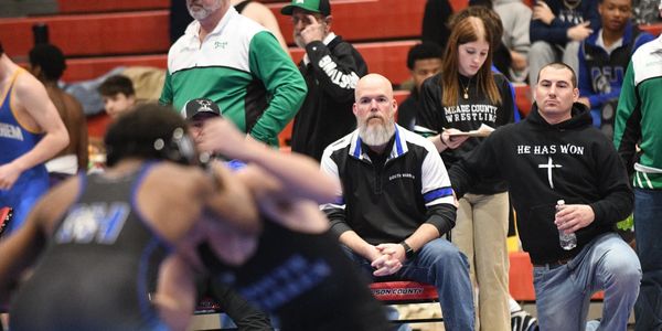 Coaches intensely watch a wrestling match in a crowded gymnasium.