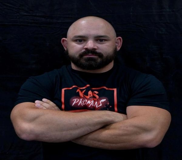 Muscular bald man with beard standing confidently with crossed arms.
