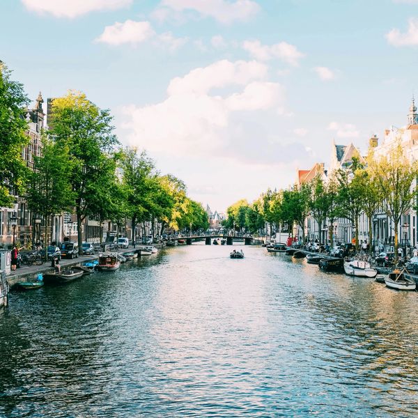 Scenic canal lined with trees and boats under a blue sky.