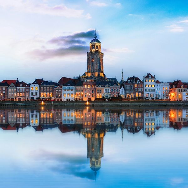 Cityscape with historic buildings reflected in calm water at dusk.