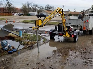 Machine working on a flooded street near a hydrant and a tipped road sign.