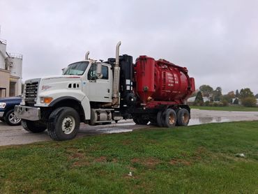 A large white and red vacuum truck parked on a gravel road beside grass.