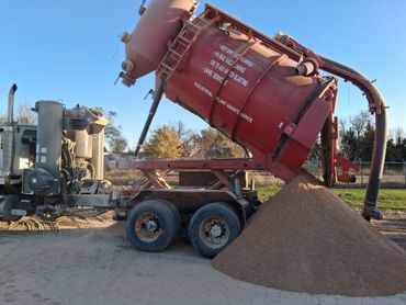 Large red industrial vacuum truck unloading sand outdoors.
