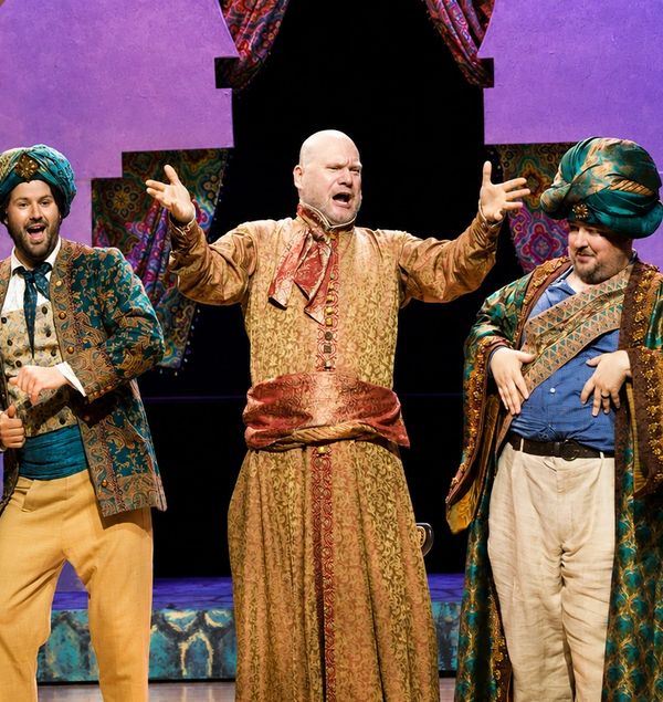 Three actors in colorful costumes performing on stage.