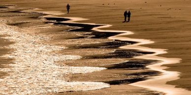 Golden sunset lights up zigzag shoreline with three people walking on the beach.