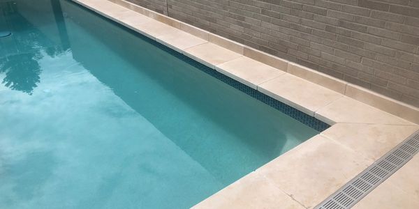 A clean swimming pool with beige tiles and a brick wall.