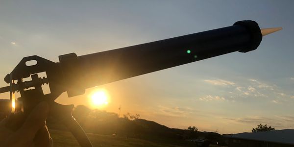 A caulking gun held against a sunset background outdoors.