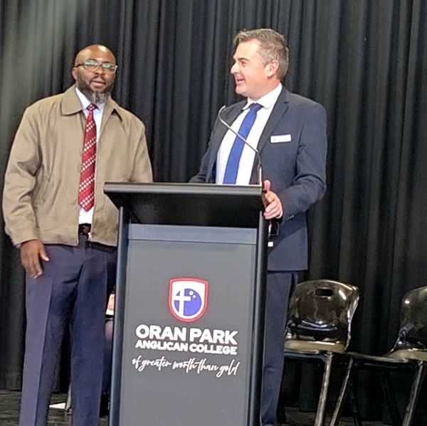 Two men standing at a podium at Oran Park Anglican College event.